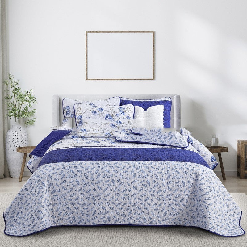 Blue and white floral bedding set on a bed in a bedroom with a plant and framed picture.